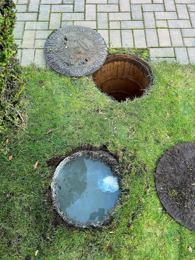 An open manhole overflowing with water, showing a blocked outside drain.
