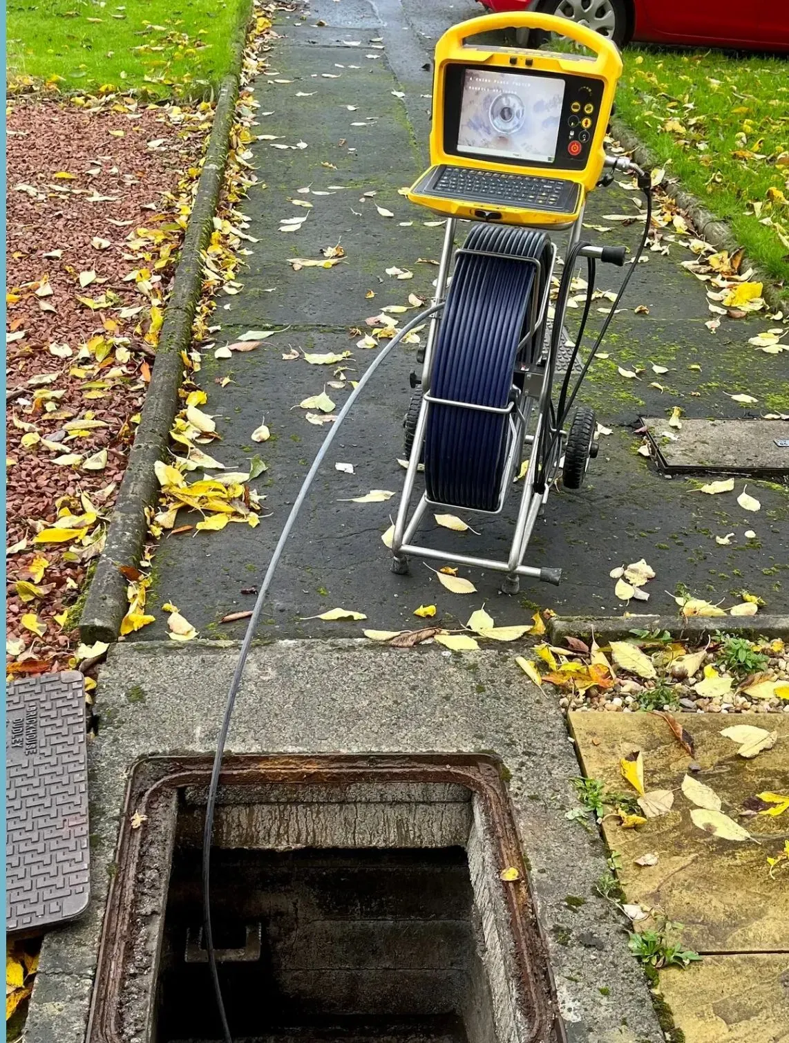 A CCTV drain survey camera next to an open manhole